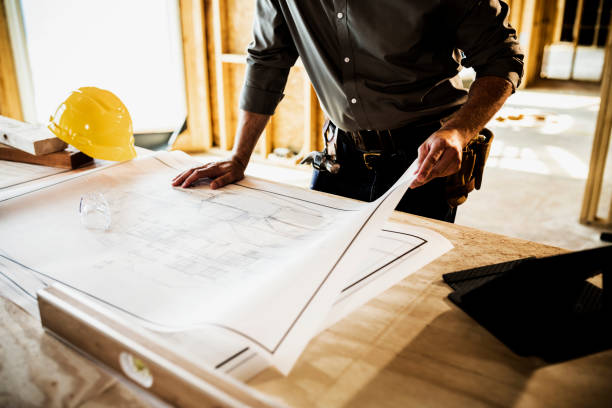 Building contractor looking over blueprints at home construction site.